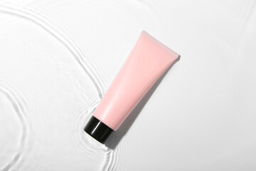 Wall Mural - Cosmetic product. Tube with cream in water on light background, top view