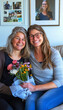 © sennauli - Two Women Smiling and Holding Flowers on a Couch