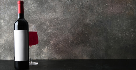 Bottle and glass of red wine on grey grunge background with space for text