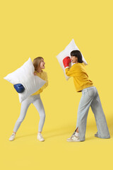 Canvas Print - Young women in boxing gloves fighting pillows on yellow background