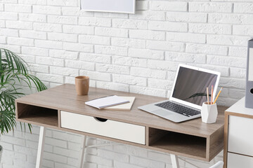 Poster - Workplace with laptop, stationery and notebooks near white brick wall in office