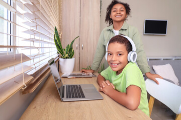 Sticker - Cute happy African-American children in headphones watching cartoons on laptop at home