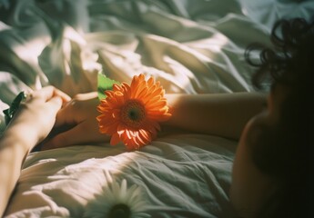 Photo of a person holding and looking at an orange flower, with the focus on their hand and arm