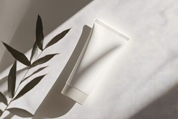 Poster - A white tube rests on a light background, with shadows highlighting a nearby leaf, creating a serene and inviting atmosphere