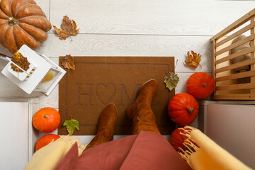 Wall Mural - Woman with pumpkins and autumn leaves standing near doormat on white wooden floor, top view