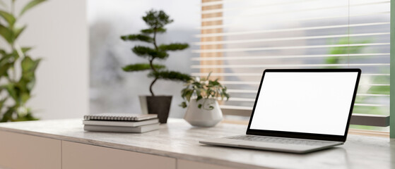 Wall Mural - A laptop white-screen mockup on a grey marble table in a contemporary bright room.