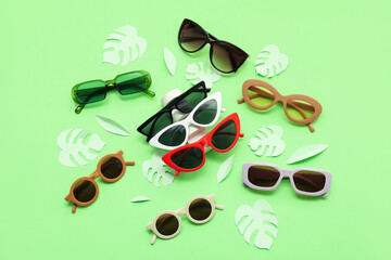 Poster - Different stylish sunglasses and palm leaves made of paper on green background