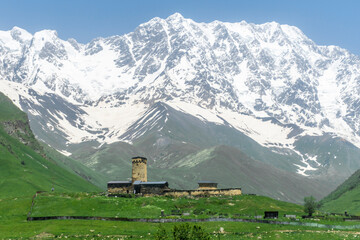 Sticker - Lamaria Monastery on a green hill. Stone medieval tower. Snow capped Mount Shkhara in the background