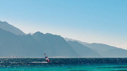 Poster - surfer rides in the Red Sea against the backdrop of high rocky mountains and a blue sky with clouds in Egypt Dahab