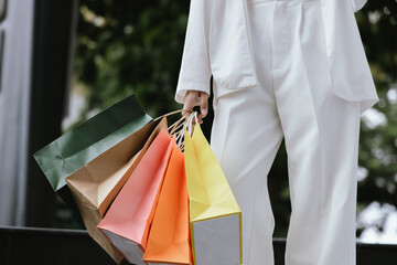 A stylish Asian woman walks happily through a modern city shopping mall. She’s holding luxury bags, enjoying the bustling urban atmosphere, surrounded by fashionable stores and other cheerful shoppers