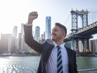 A successful businessman raises his hand in triumph, his image superimposed on a cityscape	