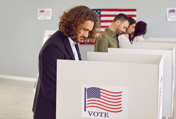 Wall Mural - Side view portrait of a young american voter man voting and putting his ballot in bin on election day standing at vote center. Diverse American citizens people standing in voting booth.