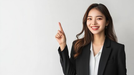 Happy young Asian business woman in blazer pointing finger up isolated on white background