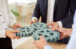 © Studio Romantic - Business people standing connecting cogs wheel, hands close-up. Concept of partnerships in business, algorithm, mechanism. The process of joining a company, merger. Group of entrepreneurs