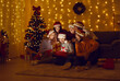 © Studio Romantic - Happy young people discover wonderful present. Mixed race multiethnic friends open gift box with magic surprise while sitting in dark living room interior with Christmas tree at Xmas gathering at home