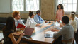 © Monkey Business - Young Businesswoman Giving Presentation To Multi-Cultural Team Sitting Around Table In Modern Office