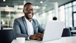 © halo - A happy Black businessman working on his laptop in an office.