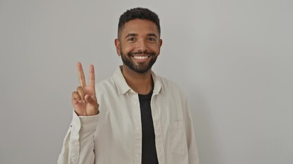 Poster - Victorious young african american man smiling, flashing peace sign, wearing a shirt, standing alone over isolated white background