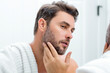 © Volodymyr - Millennial hispanic man looking in mirror, facial skin and stubble. Male beauty care product. Skincare, home spa. Beauty portrait of a beautiful man. Spa model, moisturizing nourishing creme.