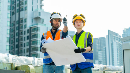 Wall Mural - Professional Asian man and woman teamwork engineer and foreman using blueprint working outdoor at construction site building rooftop. Architecture inspector inspect building exterior structure system.