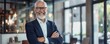 © hassan - Handsome mature businessman smiling with arms crossed in a modern office, realistic photo style.