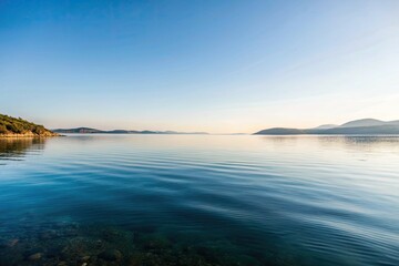 Wall Mural - Tranquil lake reflecting a serene blue sky and distant hills