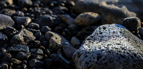 Close up of a rock with frost on it over a pile of smaller stones