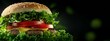 © Wall - A cheeseburger on a bun with lettuce, tomato, and a single lettuce leaf against a black backdrop