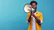 © KotBaton - Emotional young black guy making announcement with megaphone in hands, cheerful african american man using loudspeaker to share news on blue background with copy space.