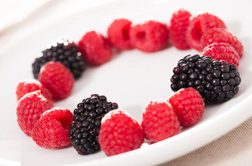 Raspberries and blackberries laid out on a white plate in circle