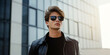 © HelgaQ - Stylish Young Man in Black Leather Jacket and Sunglasses Against Modern Glass Building