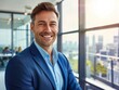 © hassan - Businessman in a blue suit, smiling at the camera, close-up portrait against a modern office interior and cityscape view, copy space on the right.