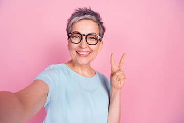 Poster - Portrait of nice aged lady selfie v-sign blue t-shirt isolated on pink color background