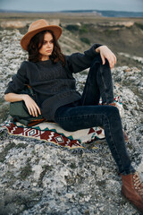 Wall Mural - Serene woman in hat sitting crosslegged on rock with hands on knees overlooking scenic view