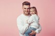 © Антон Сальников - Father lifting daughter, smiling at each other, showcasing love and happiness against pink studio backdrop. Fatherhood joy concept.