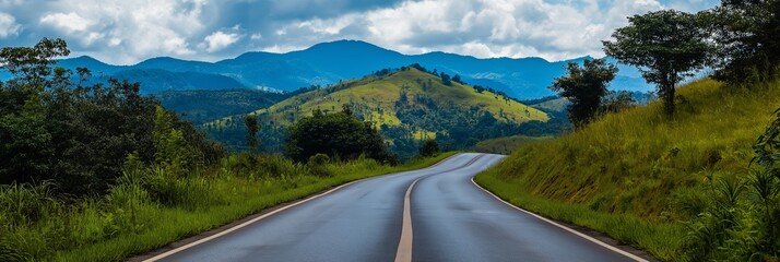 A picturesque and tranquil road winds through lush green hills and trees, leading towards a beautiful mountainous horizon.