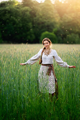 Beautiful blonde long braided hair girl in Ukrainian traditional dress  posing near old houses on nature . Portrait of young smiling attractive woman in accessories  .