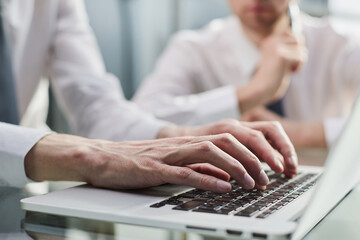 Closeup view of two young coworkers working on mobile laptop computer at office