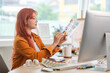 © wattana - Young graphic designer with red hair examining a color swatch in a creative office.