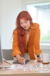 © wattana - Young stylish woman, graphic designer with red hair examining a color swatch in a creative office.