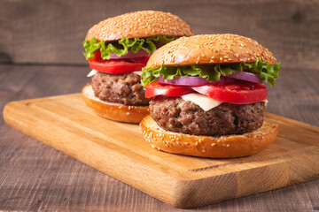 Homemade delicious hamburger with beef, onion, tomato, lettuce and cheese. Fresh burger close up on wooden rustic table with potato fries. Cheeseburger. Burger.