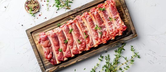 Wall Mural - Top-down view of raw pork spare ribs on a kitchen tray with herbs on a white background, featuring copy space image.