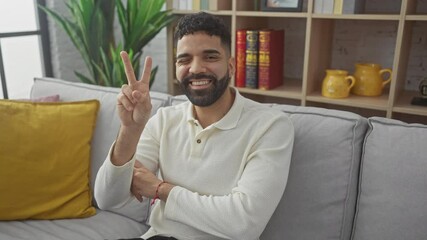 Poster - Young hispanic man at home, winking and smiling with a happy face, showing a victory sign with two fingers for a win