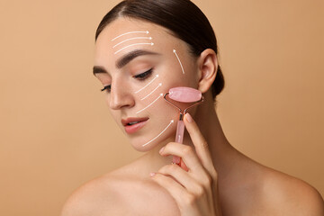 Poster - Beautiful young woman doing facial massage with roller on dark beige background. Lines on skin showing directions of motion