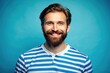 © Achiraya - Happy bearded man in a bright blue striped shirt looks aside, flashing a warm and friendly smile against a clear blue studio background.