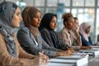 © Yuliia - group of diverse business women sitting around a conference table, discussing documents and planning a project, with a senior manager offering guidance and mentorship to an intern worker.