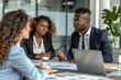 © Yuliia - photo of a diverse group of business professionals gathered around a conference table, discussing project updates and KPI reviews. A black man in a suit is seen talking to a woman client