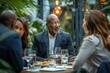 © Yuliia - photo of a diverse group of business professionals gathered around a conference table, discussing project updates and KPI reviews. A black man in a suit is seen talking to a woman client