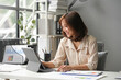© amnaj - Asian businesswoman is smiling while working from her home office and using a tablet to review some charts