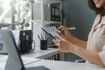 Poster - Businesswoman taking notes on a clipboard while examining financial charts at her desk in her office